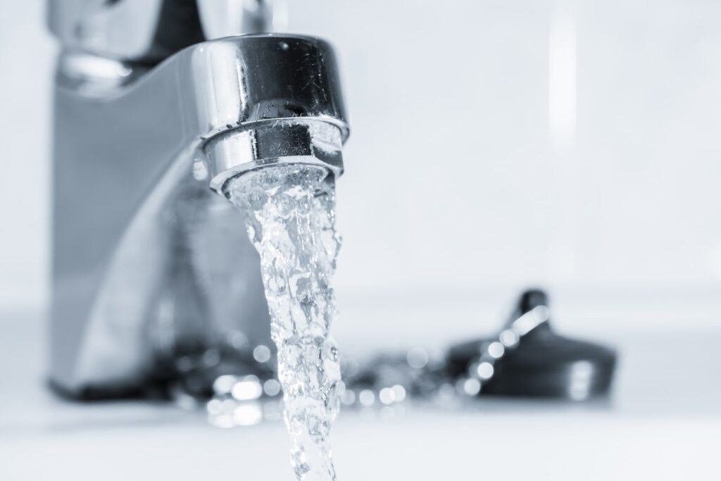 A close-up of a metallic faucet with water pouring out into a basin, accompanied by a chain and plug stopper.