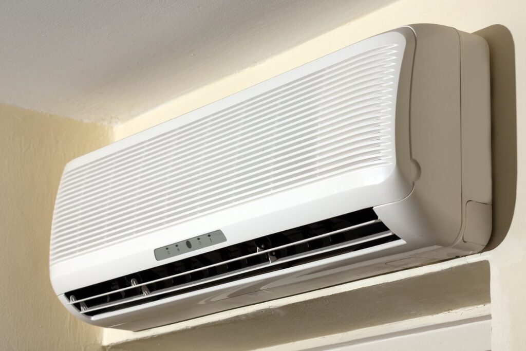 Wall-mounted white air conditioning unit with visible vents and control buttons, installed near the ceiling.
