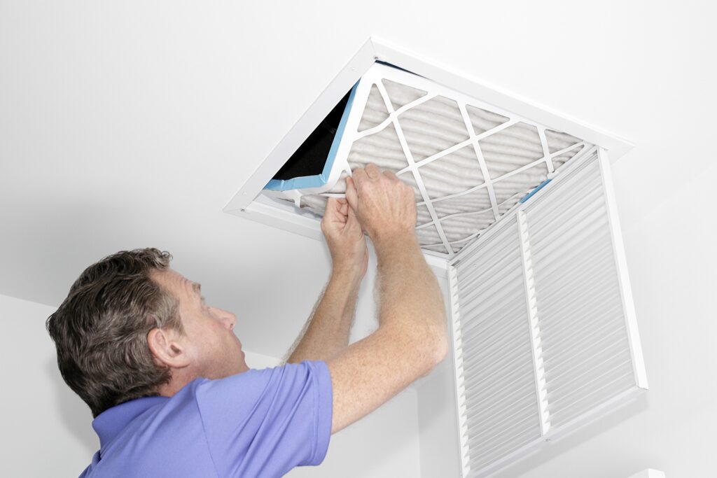 A HELP team member in a blue shirt replaces an air filter in a ceiling vent, ensuring clean air and customer comfort.
