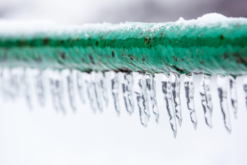 ice and icicles around green pipe in the winter