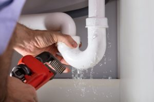 plumber holding red tool to white curved leaking pipe under sink 