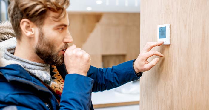 man changing temperature on thermostat in modern home with hoodie and sweatshirt on 