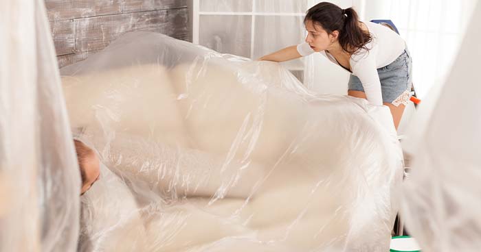 During a home repipe, you'll need to cover your furniture with plastic sheets, similar to the woman in this photo.