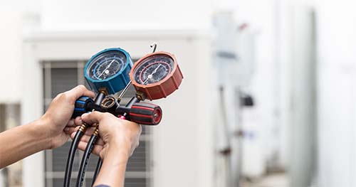 Image: an air conditioner technician uses a tool to read levels of an AC unit.