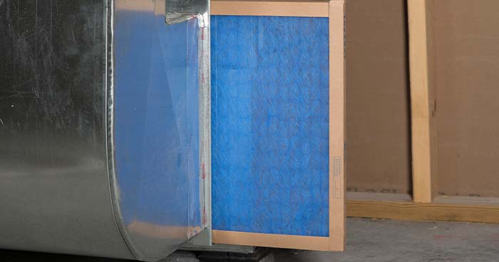 Image: A blue air filter sticks out of it's home in a furnace. You can find the HVAC filter size by measuring inside the chamber that holds the filter.