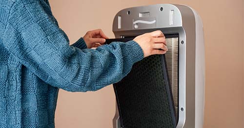 Image: a woman changing the filter in an air purifier.