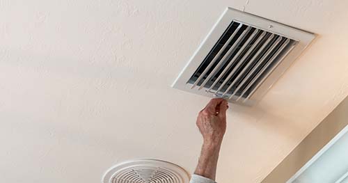 Image: a person adjusting a vent in their home.
