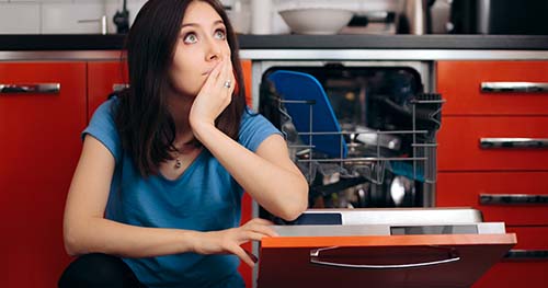 Image: a woman sits by her broken dishwasher.