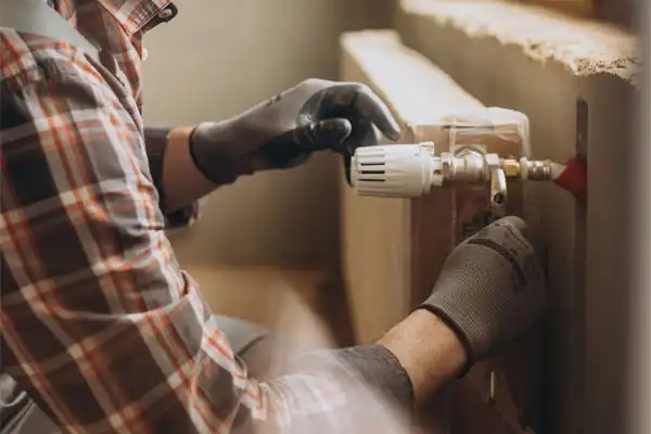 A person wearing gloves adjusts a radiator valve with a wrench.