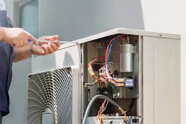 Technician using tools to repair an open air conditioning unit, with exposed wires and components visible.