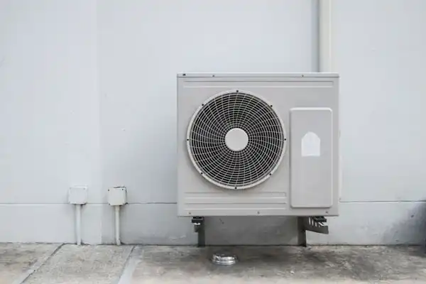 Outdoor air conditioning unit installed on a white wall, with piping and cables adjacent.