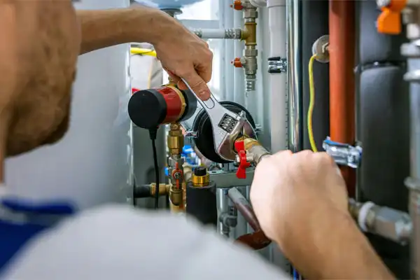 A plumber uses a wrench to adjust a valve on a complex network of pipes in a utility room.