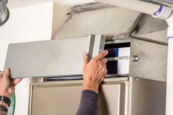 Hands are seen removing a metal panel from an HVAC unit for maintenance, exposing the interior components.
