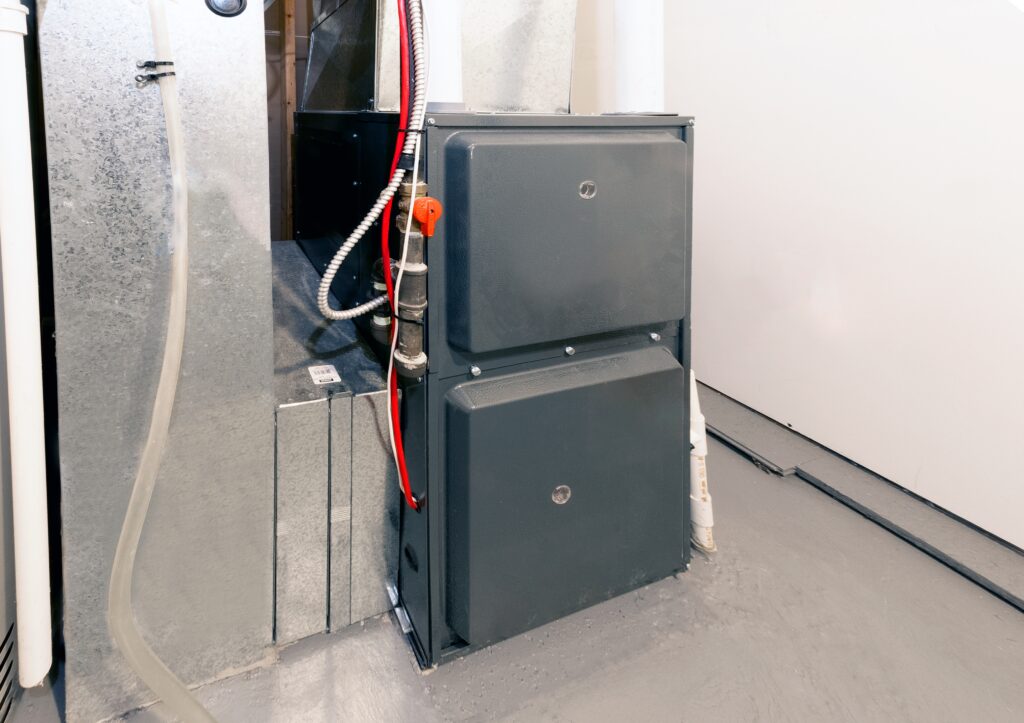 A gray HVAC furnace installed in a HELP team-serviced basement, featuring wiring, ductwork, and insulated pipe connections.