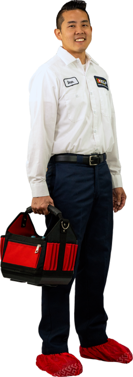 Person in a white uniform shirt holding a black and red tool bag, wearing red shoe covers, standing and smiling.